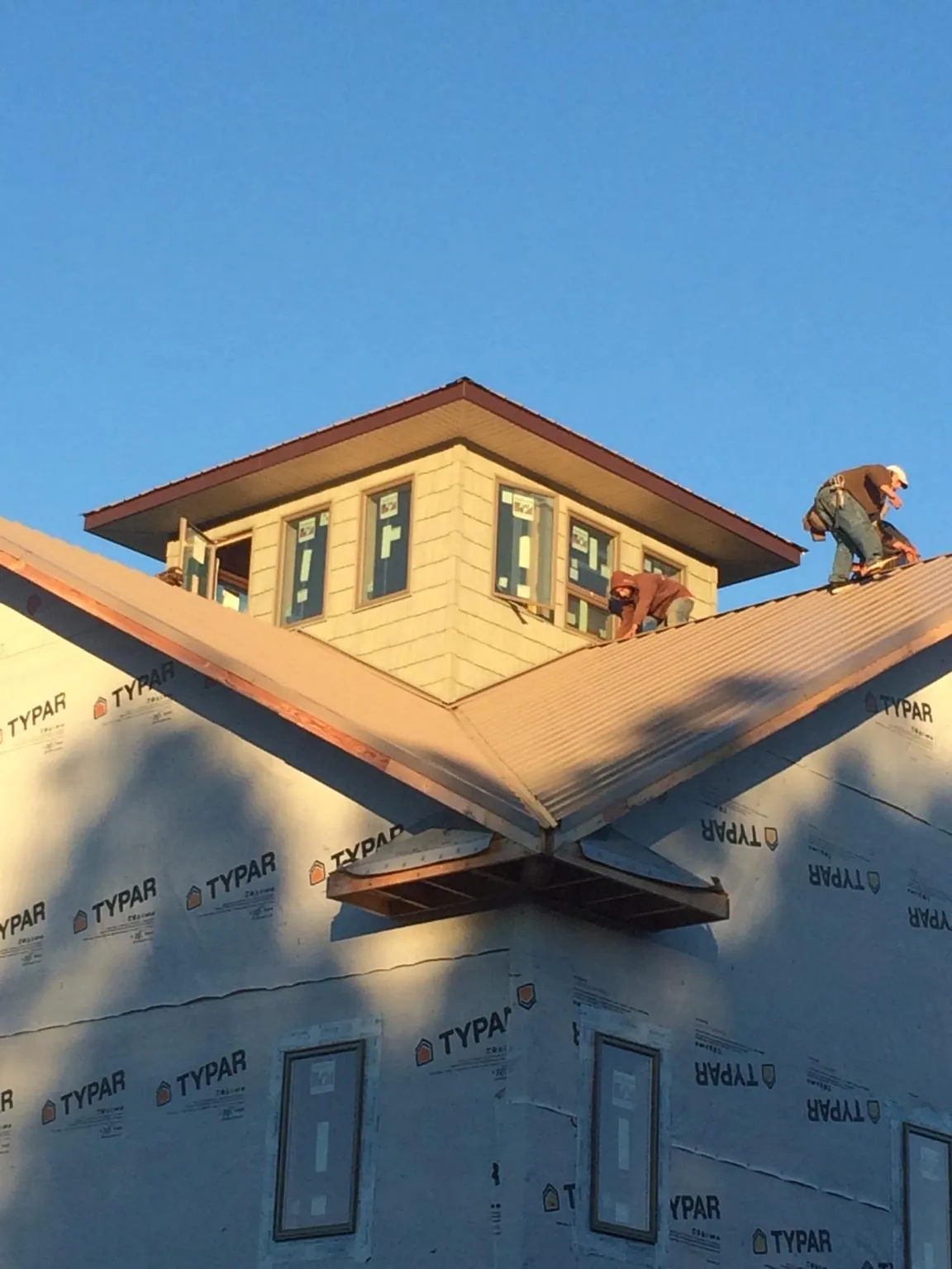 Roofers working around a rooftop cupola on a new metal roof at sunset — Roof Waterproofing in Waltham by Roofing Brothers